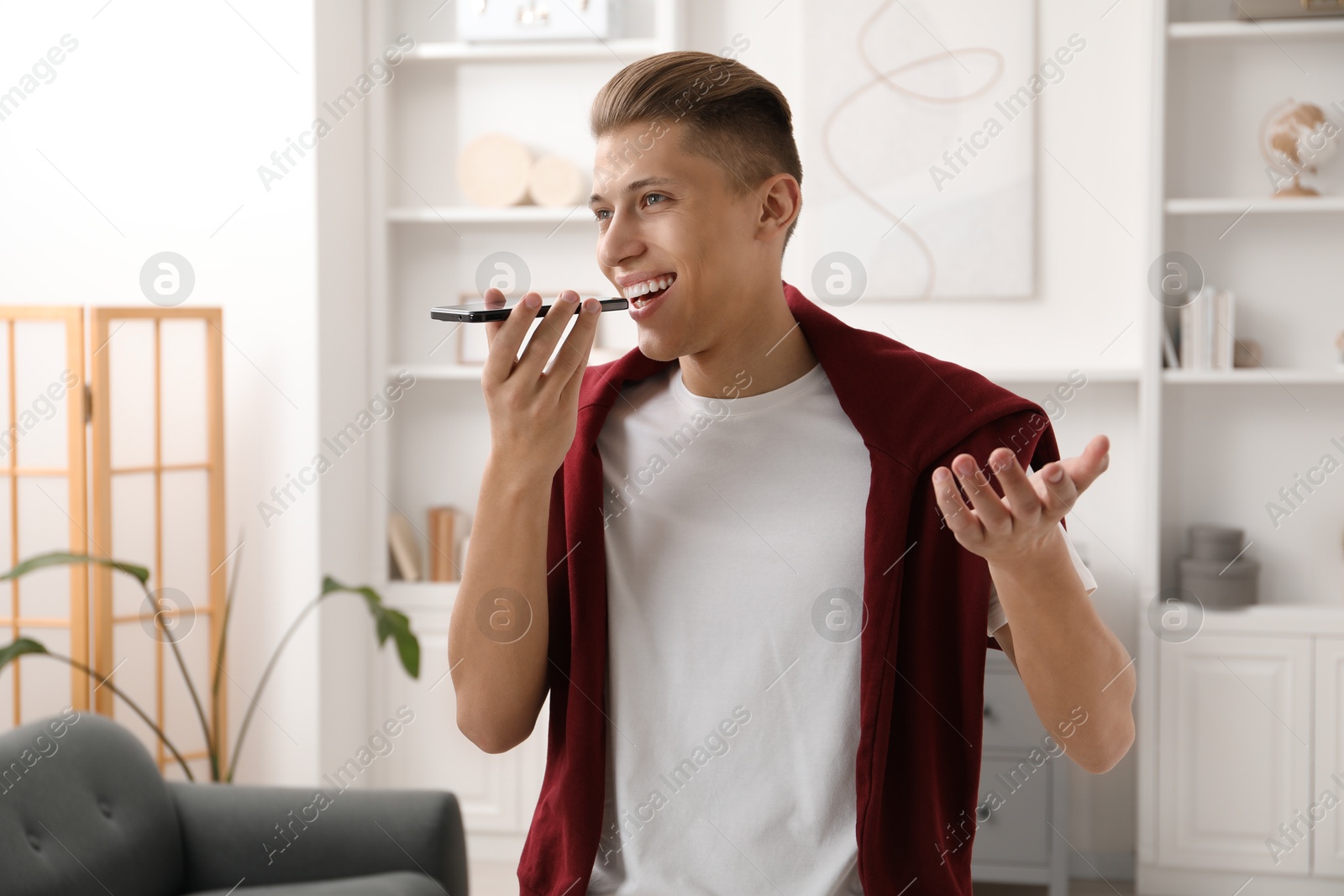 Photo of Young man recording voice message via smartphone at home