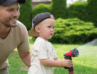 Father and his son watering lawn with hose in backyard