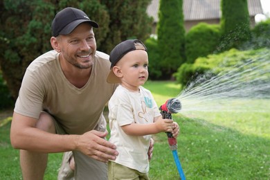 Photo of Father and his son watering lawn with hose in backyard