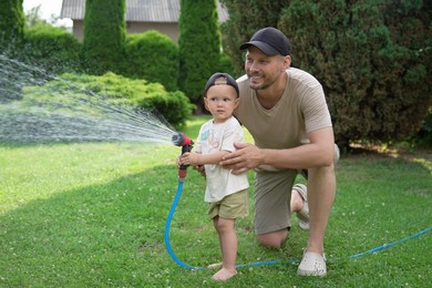 Photo of Father and his son watering lawn with hose in backyard