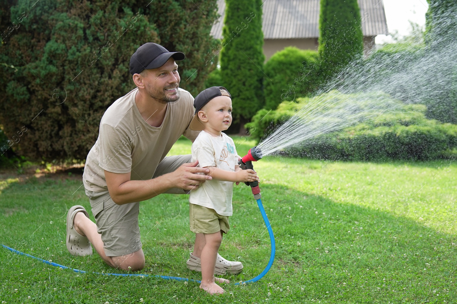 Photo of Father and his son watering lawn with hose in backyard