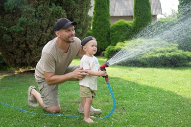 Father and his son watering lawn with hose in backyard