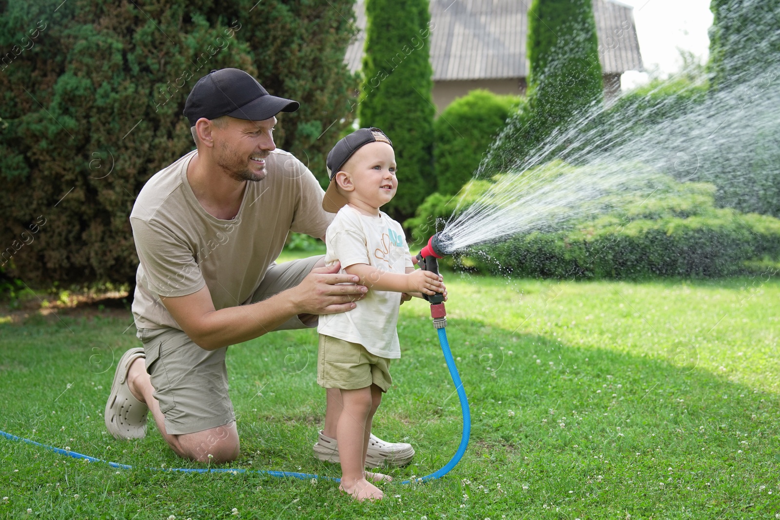 Photo of Father and his son watering lawn with hose in backyard