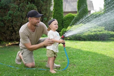 Father and his son watering lawn with hose in backyard