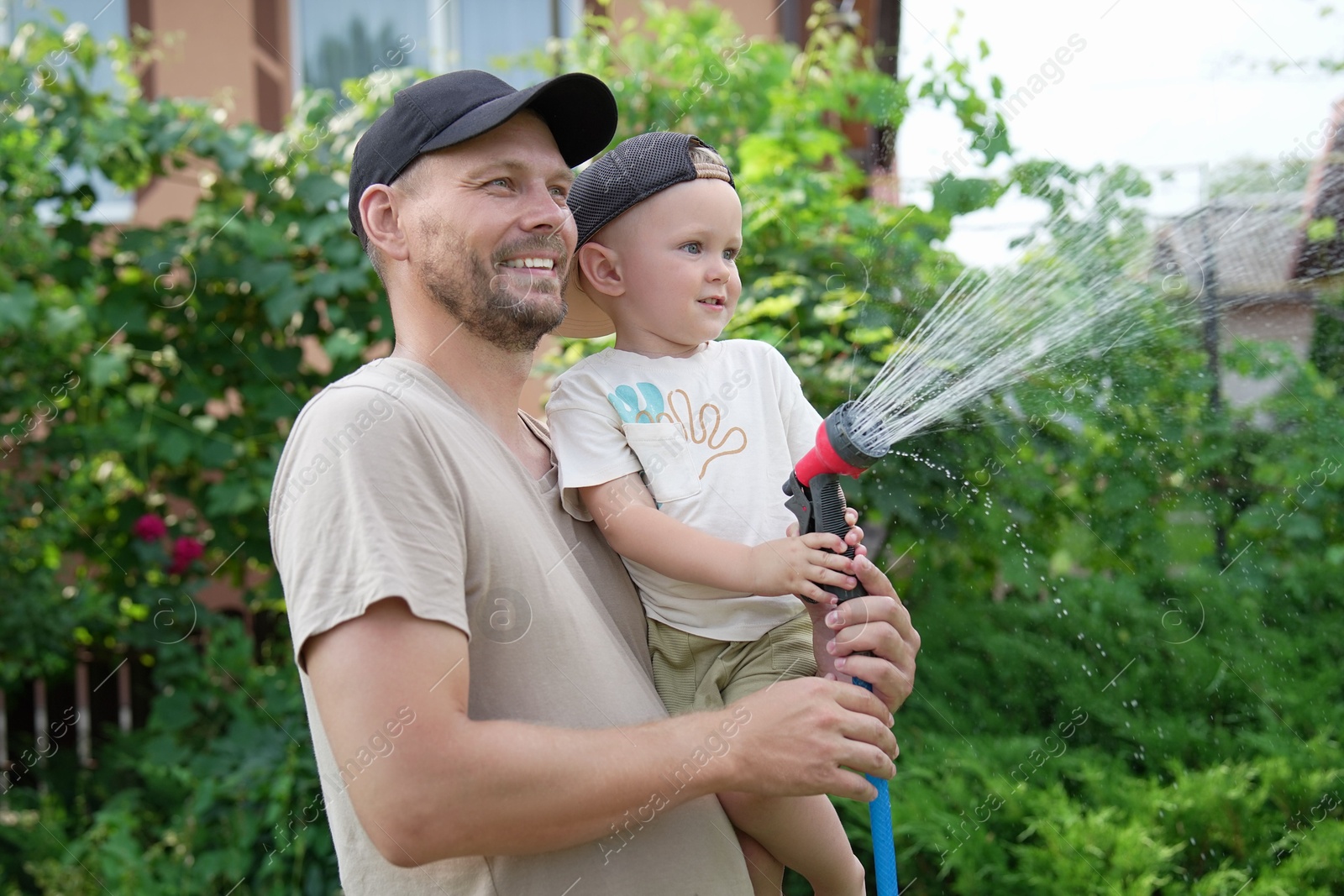 Photo of Father and his son watering lawn with hose in backyard