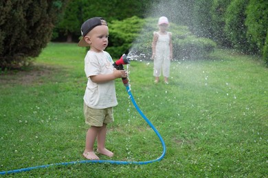 Photo of Little boy and his sister watering lawn with hose in backyard