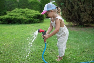 Photo of Little girl watering lawn with hose in backyard