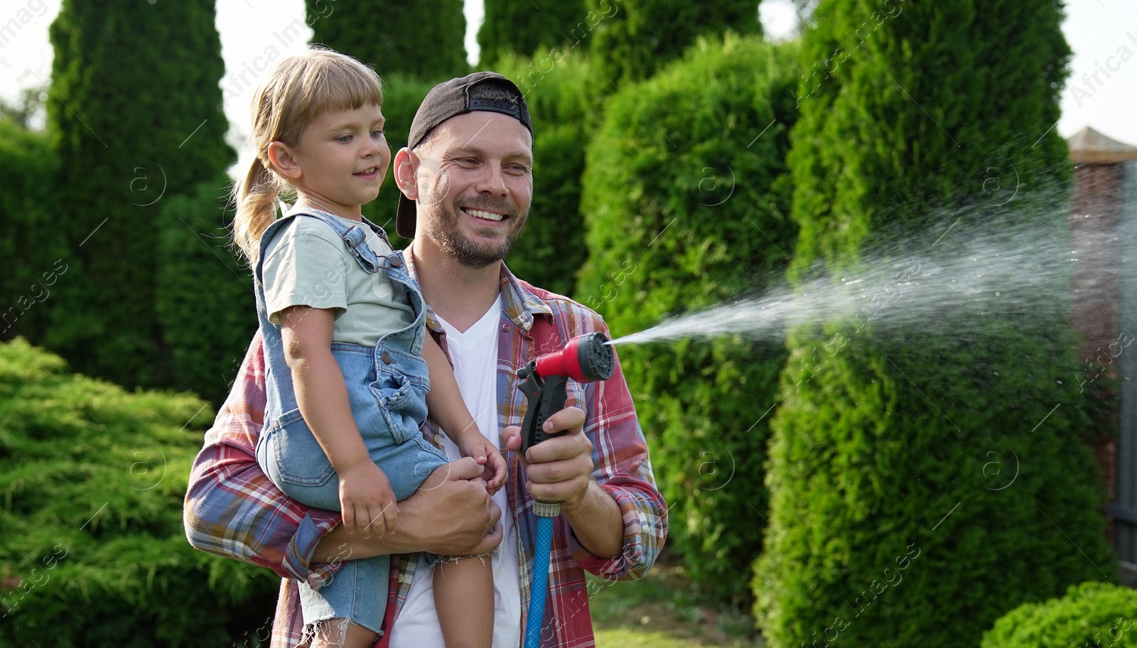 Photo of Father and his daughter watering lawn with hose in backyard