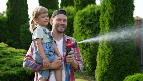 Father and his daughter watering lawn with hose in backyard