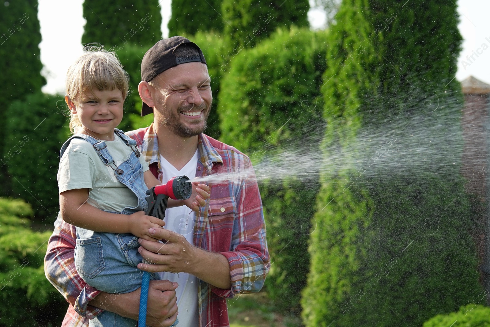 Photo of Father and his daughter watering lawn with hose in backyard