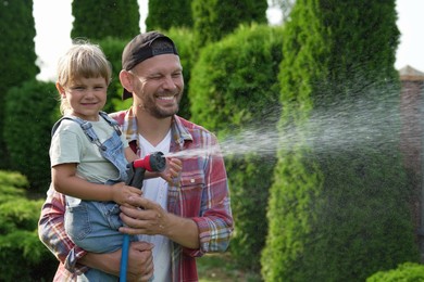 Photo of Father and his daughter watering lawn with hose in backyard