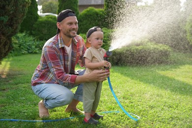 Father and his son watering lawn with hose in backyard