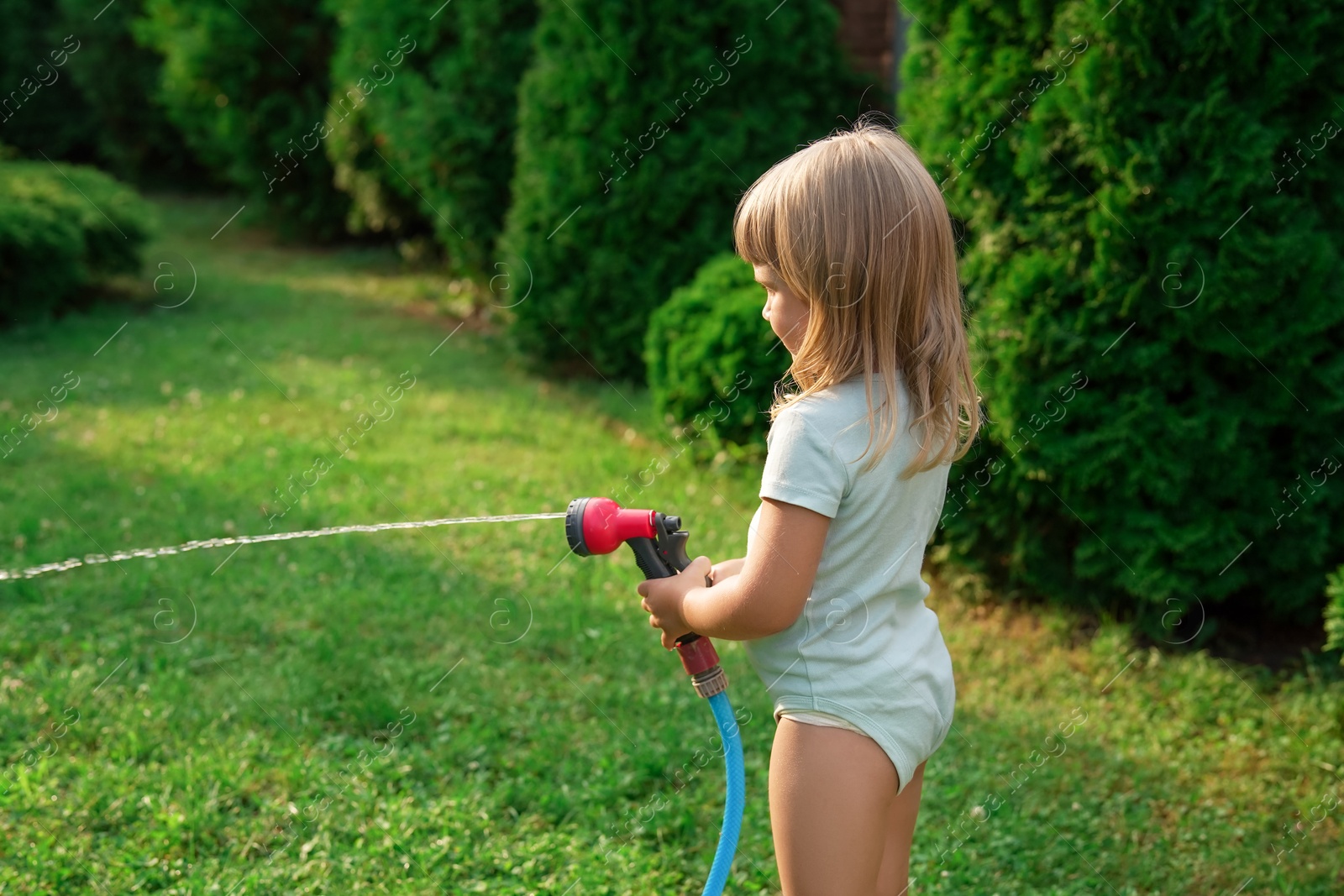 Photo of Little girl watering lawn with hose in backyard