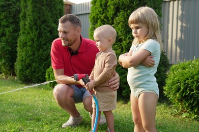 Little boy watering lawn with hose while his father and sister watching in backyard, selective focus