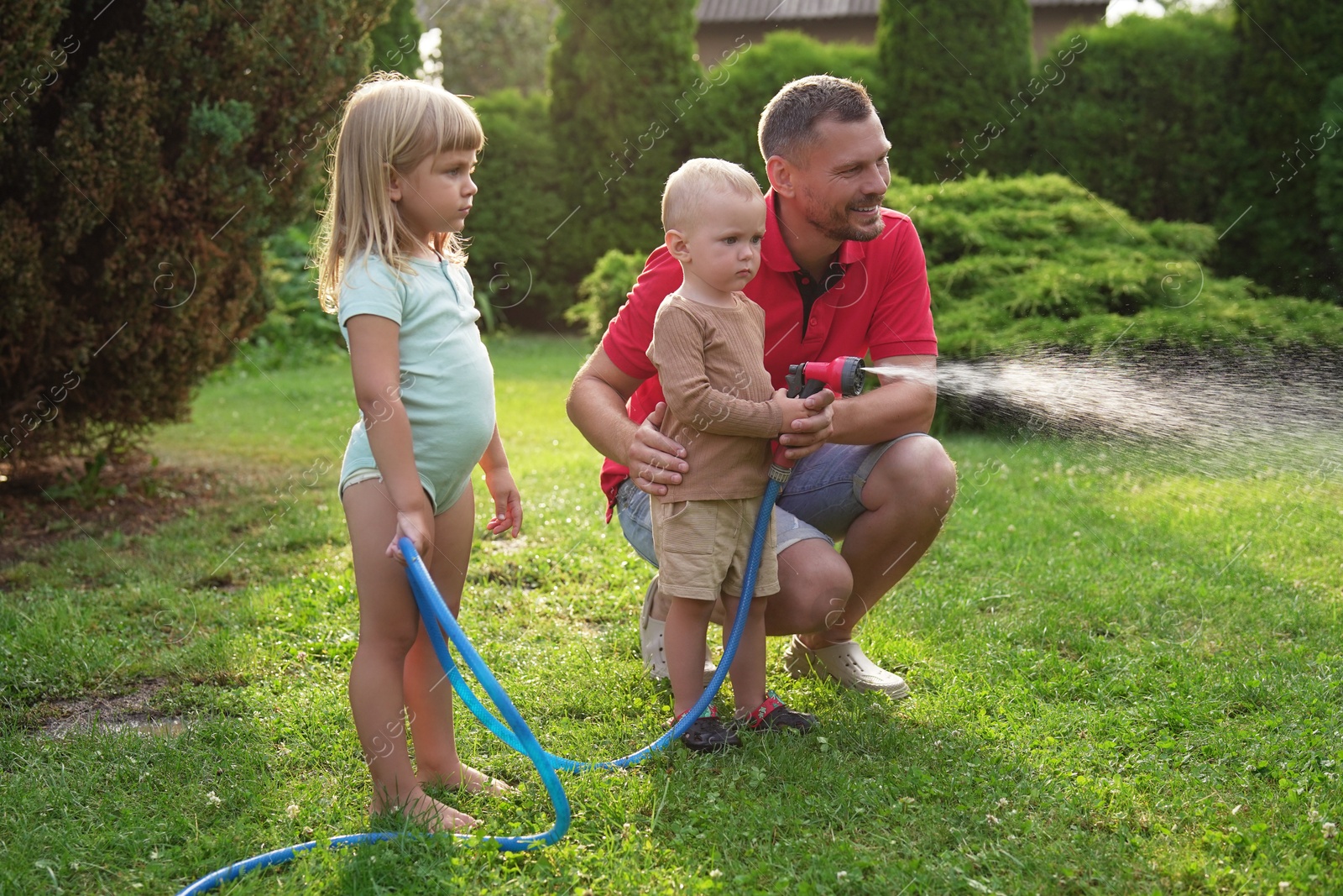 Photo of Little boy watering lawn with hose while his father and sister watching in backyard