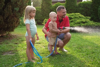 Little boy watering lawn with hose while his father and sister watching in backyard