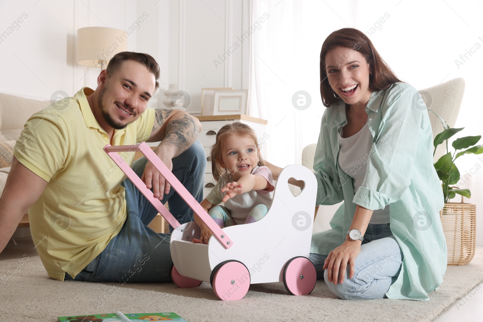 Photo of Happy family. Parents and their cute little daughter in wooden stroller at home