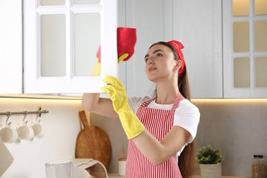 Beautiful young woman cleaning furniture with rag in kitchen