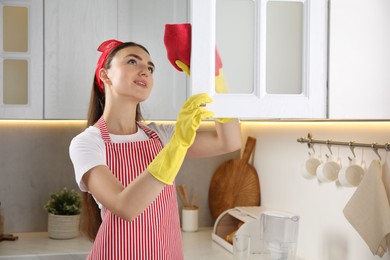 Beautiful young woman cleaning furniture with rag in kitchen