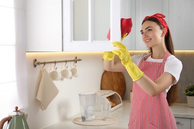 Photo of Beautiful young woman cleaning furniture with rag in kitchen