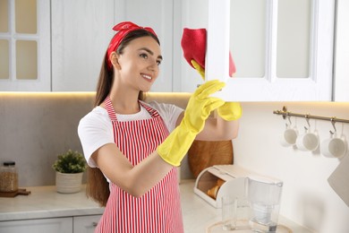 Beautiful young woman cleaning furniture with rag in kitchen