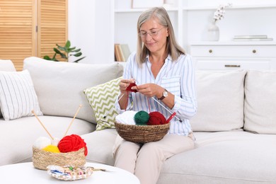 Photo of Woman with basket of yarn knitting on sofa at home