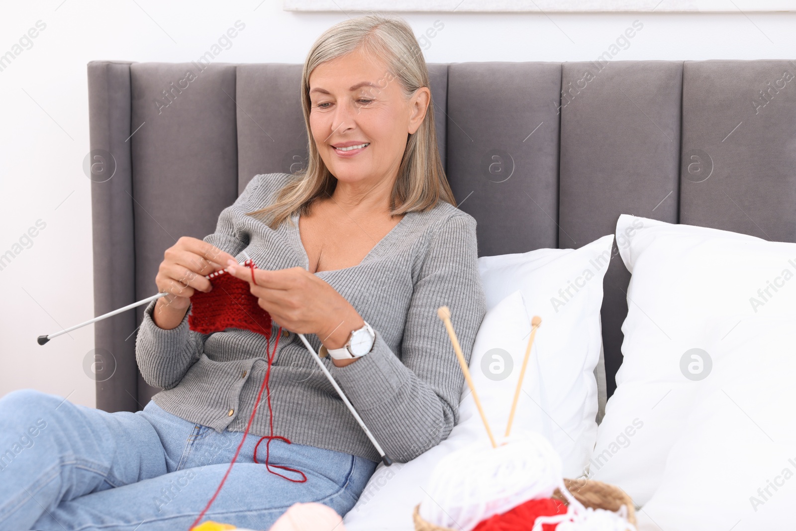 Photo of Smiling senior woman knitting on bed at home