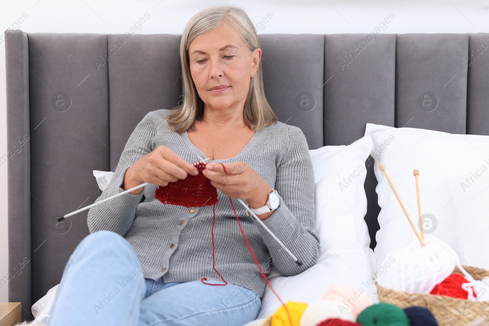 Photo of Beautiful senior woman knitting on bed at home