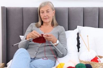 Beautiful senior woman knitting on bed at home