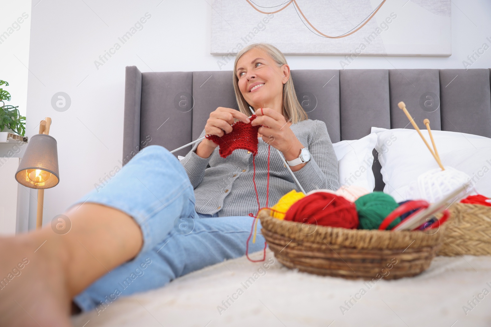 Photo of Smiling senior woman knitting on bed at home