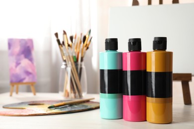 Photo of Acrylic paints of different colors, small easels, palette and brushes on wooden table indoors