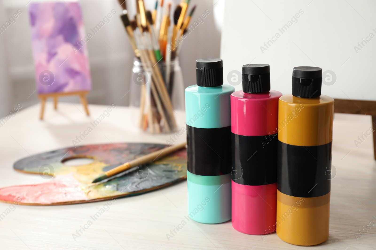 Photo of Acrylic paints of different colors, small easels, palette and brushes on wooden table indoors