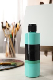 Photo of Turquoise acrylic paint in bottle, small easel, palette and brushes on wooden table indoors