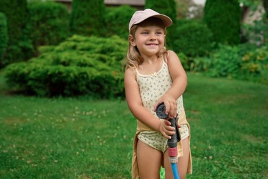 Photo of Cute little girl with hose in backyard, space for text