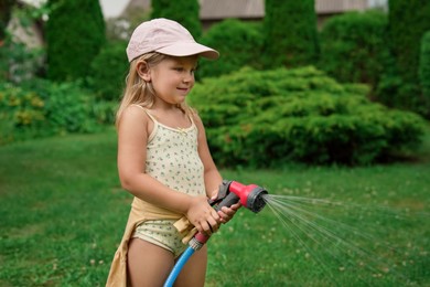 Photo of Little girl watering lawn with hose in backyard