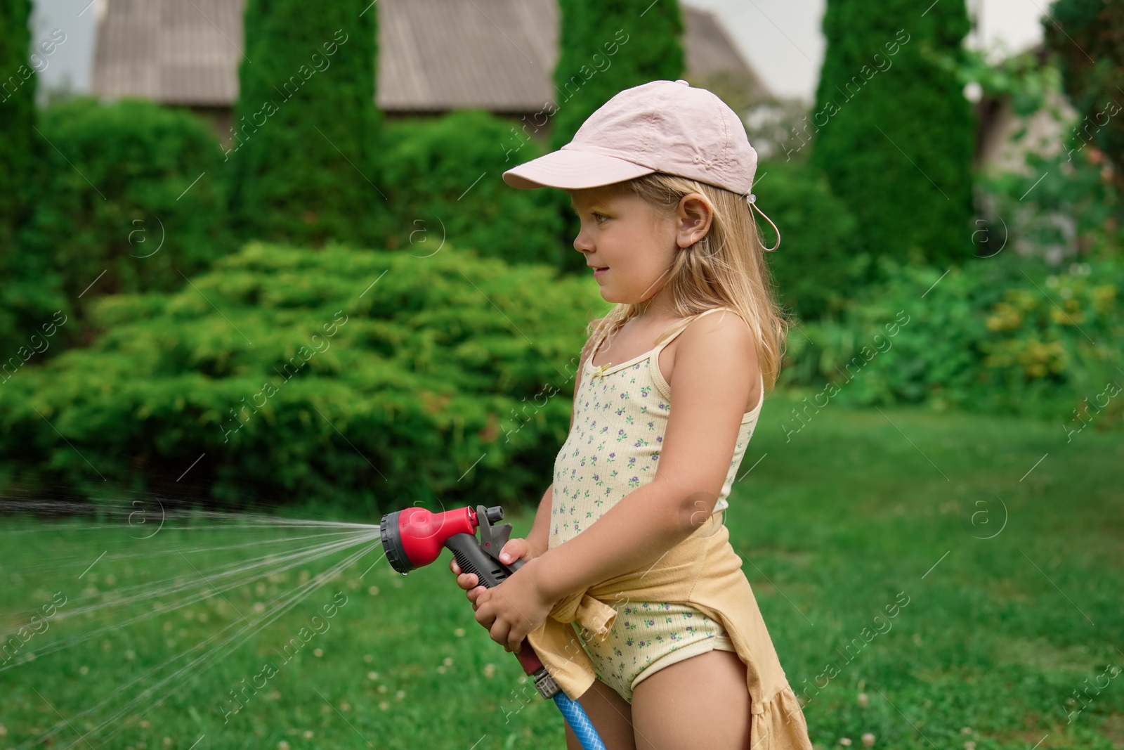 Photo of Little girl watering lawn with hose in backyard