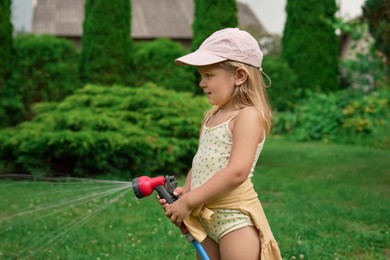 Photo of Little girl watering lawn with hose in backyard