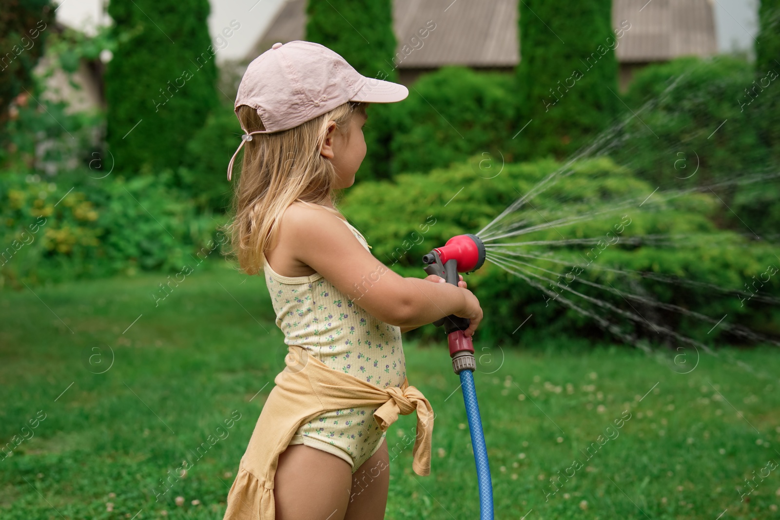 Photo of Little girl watering lawn with hose in backyard