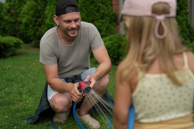 Father and his daughter watering lawn with hose in backyard, selective focus