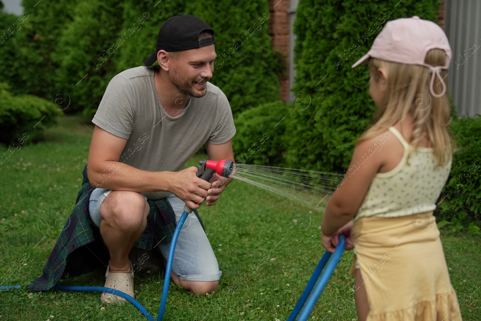 Photo of Father and his daughter watering lawn with hose in backyard, selective focus