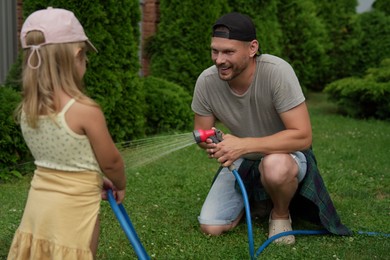 Father and his daughter watering lawn with hose in backyard, selective focus