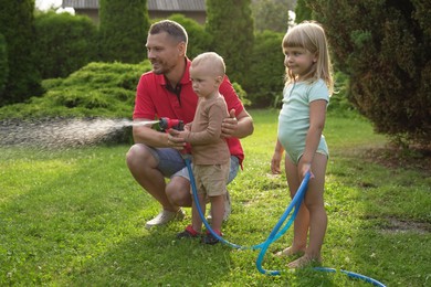 Little boy watering lawn with hose while his father and sister watching in backyard