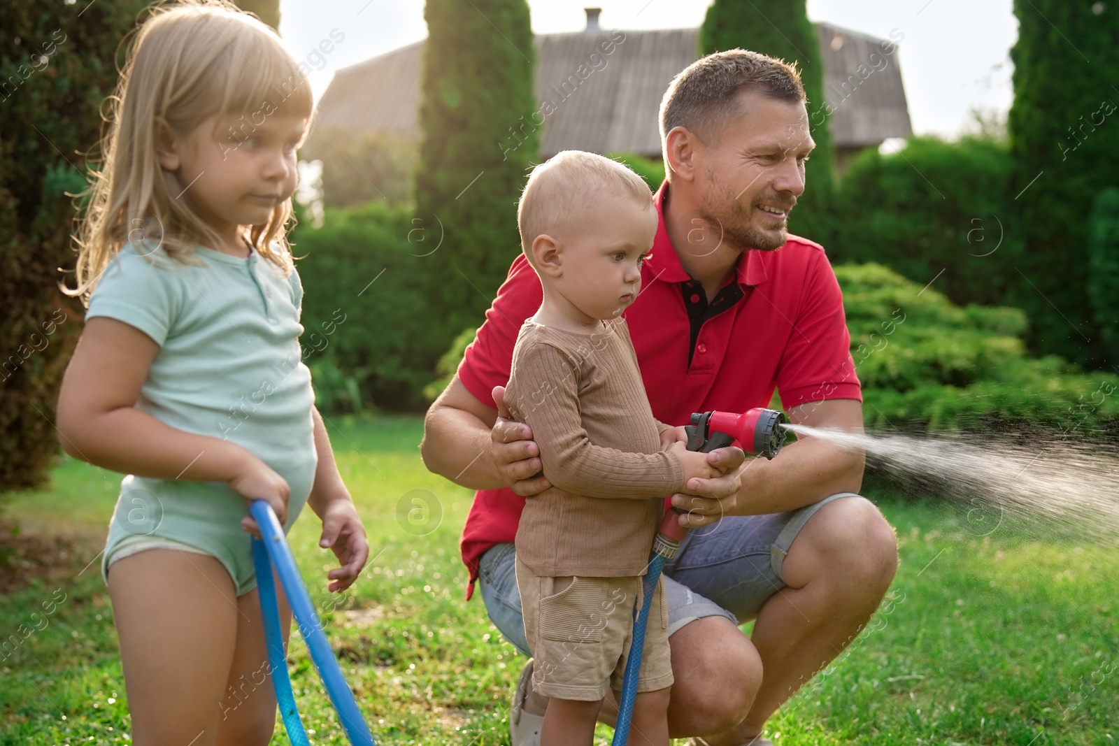 Photo of Little boy watering lawn with hose while his father and sister watching in backyard