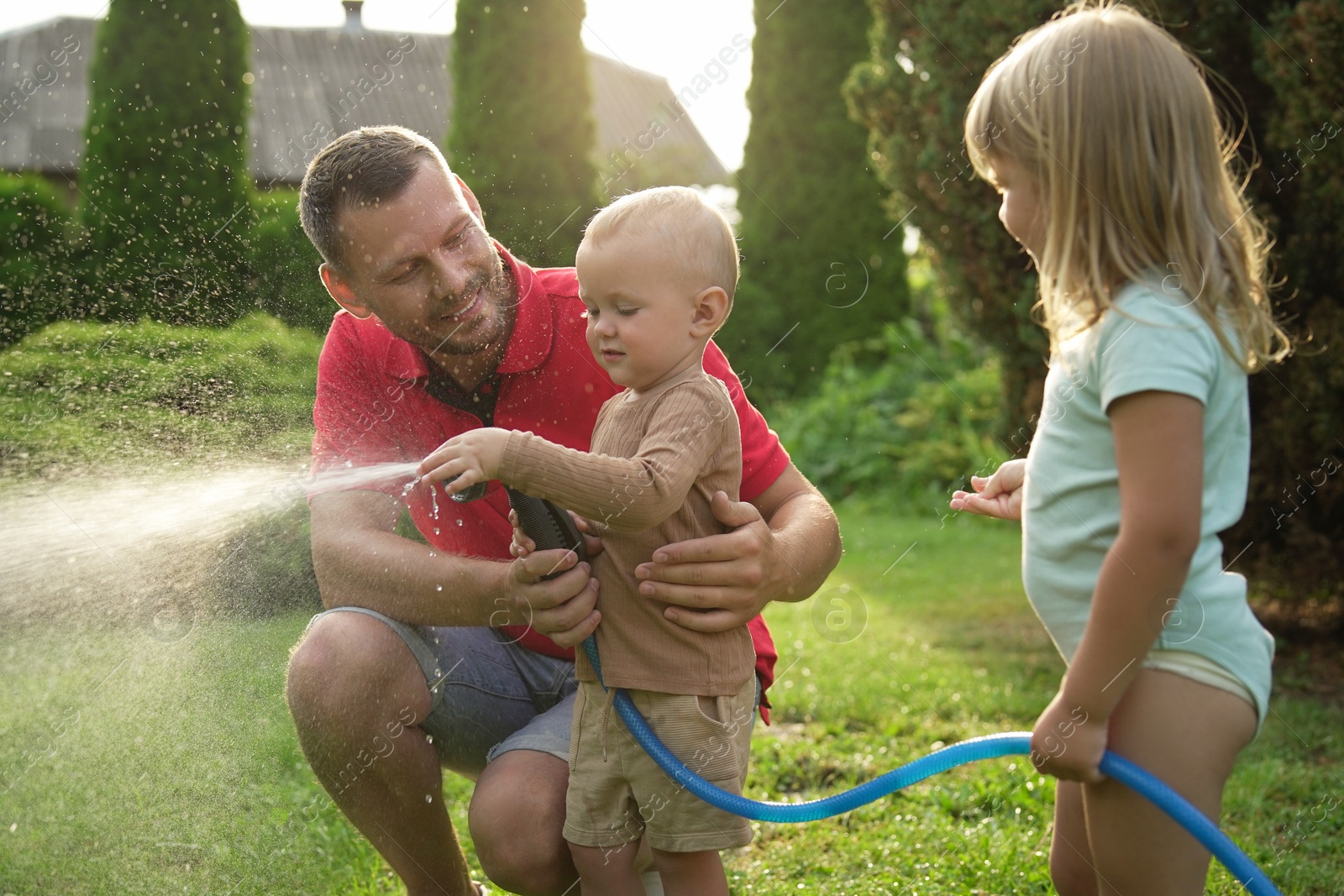 Photo of Little boy watering lawn with hose while his father and sister watching in backyard