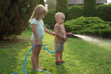 Little boy and his sister watering lawn with hose in backyard