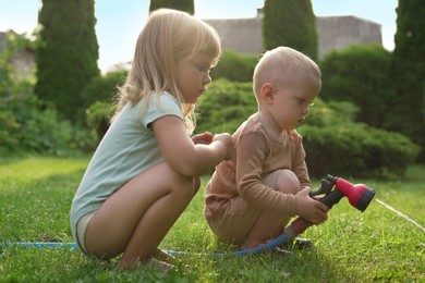 Photo of Little boy and his sister watering lawn with hose in backyard