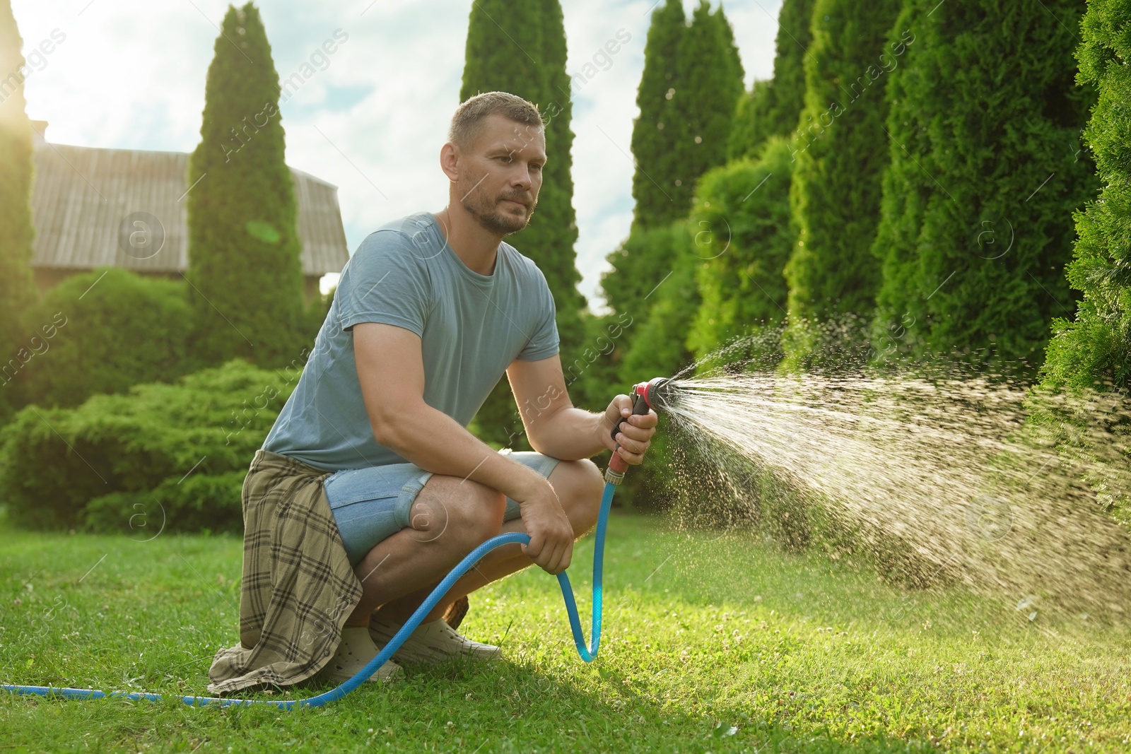 Photo of Man watering lawn with hose in backyard