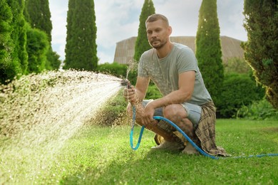 Man watering lawn with hose in backyard