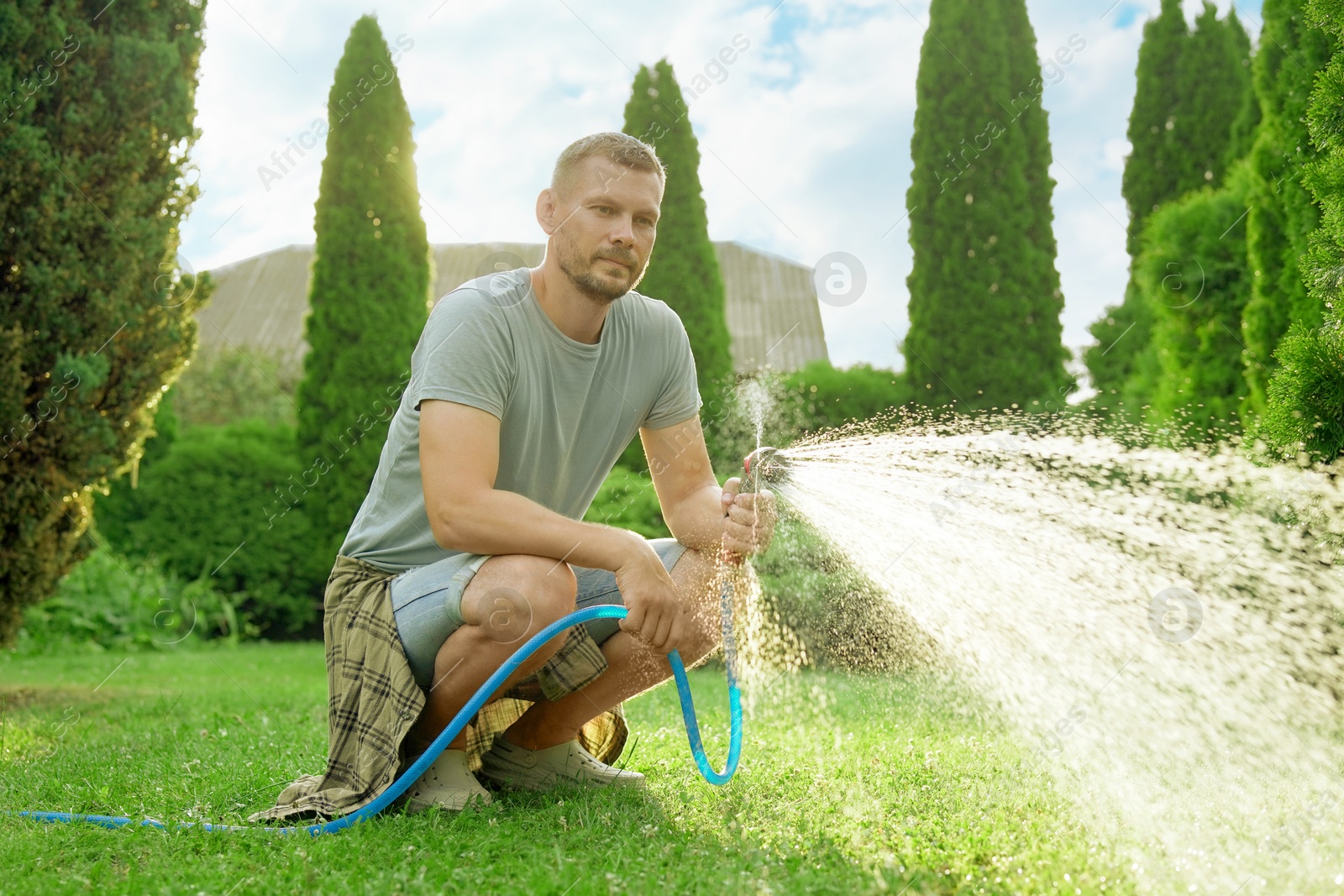 Photo of Man watering lawn with hose in backyard