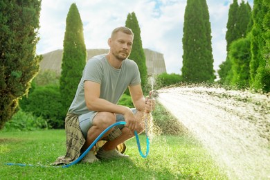 Photo of Man watering lawn with hose in backyard